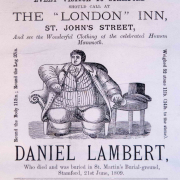 A vintage advertisement featuring an illustration of a large man seated in a chair, promoting the clothing of Daniel Lambert, who is described as a "celebrated Human Mammoth" and noted for his extraordinary size.
