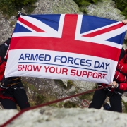 Two people in climbing gear hold the Armed Forces Day Flag
