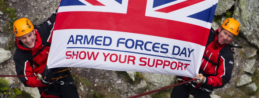 Two people in climbing gear hold the Armed Forces Day Flag