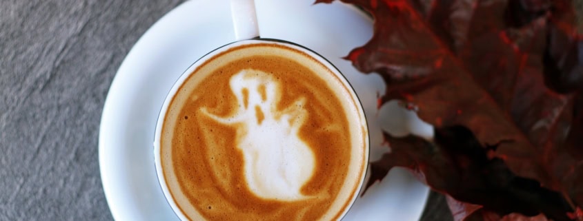 white ceramic teacup filled with ghost illustration coffee latte on white ceramic saucer beside maroon leaf photography